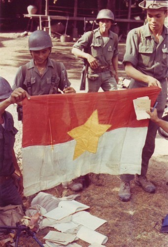 ARVN infantrymen display propaganda leaflets and a flag captured by them during a drive against Viet Cong guerrillas.