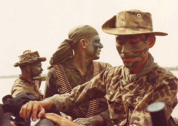 Camouflage clad SEAL team members aboard a riverine craft in South Vietnam.