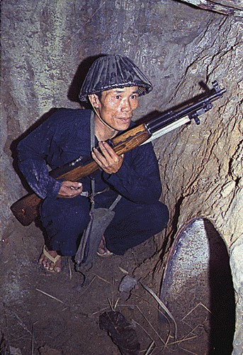 A Viet Cong soldier crouches in a bunker with an SKS carbine.